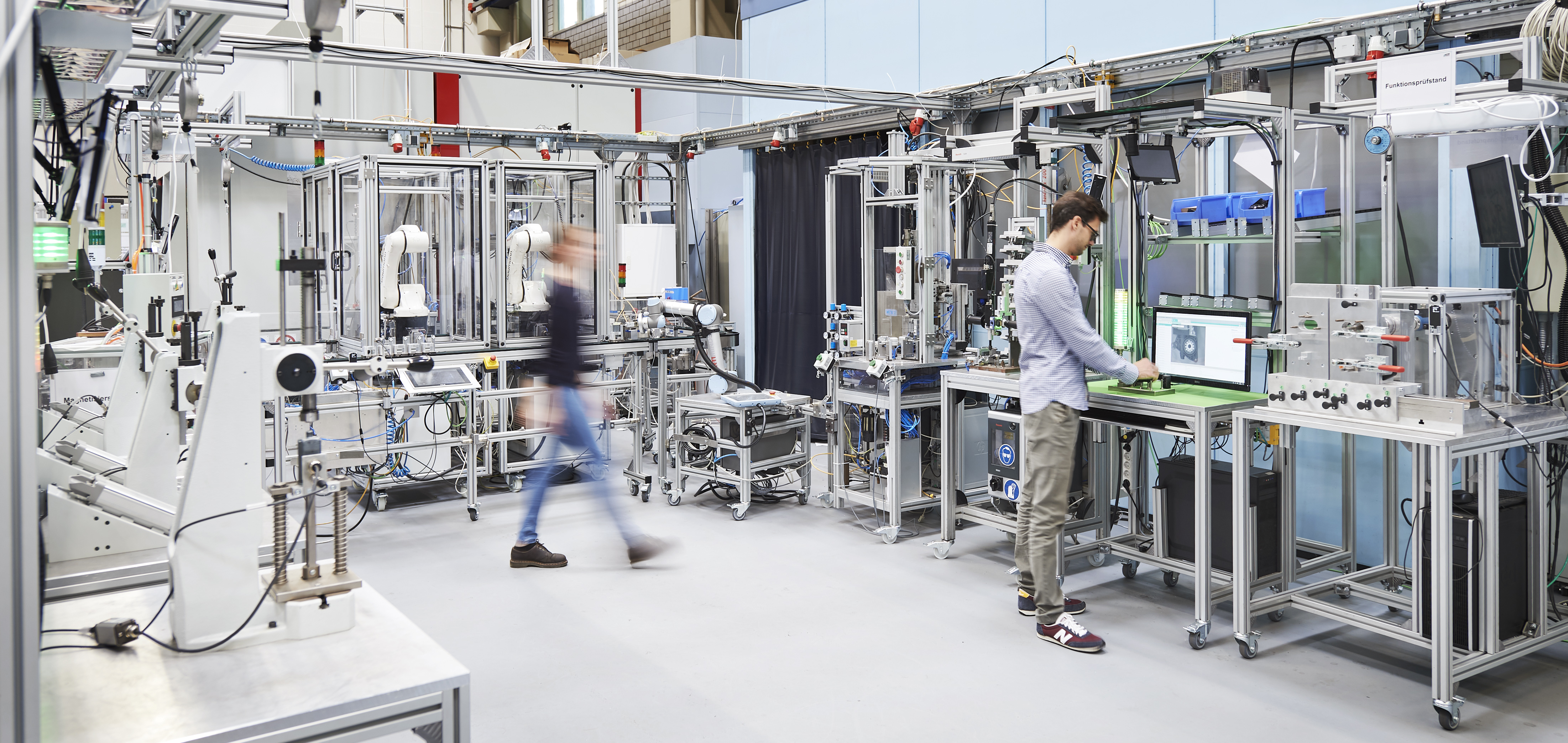 Mitarbeitende in der Lernfabrik des wbk arbeiten an vernetzten Industrie-4.0-Stationen mit Robotik und Automatisierungstechnik.